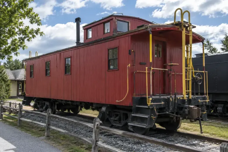 A preserved generic red wooden railway caboose on museum track viewed from a safe public path.
