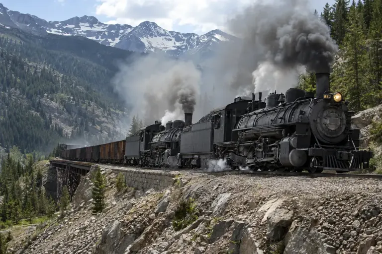 Two historically plausible steam locomotives assisting a freight train on a mountain railway.